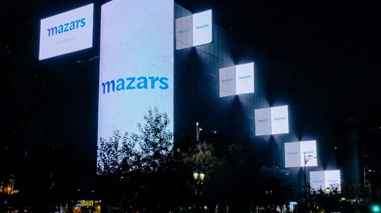 Image of a city at night featuring multiple digital screens with Mazars logo