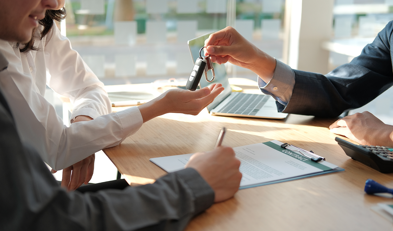 Three people mostly out of frame while their hands interact, two people are exchanging a set of car keys while the third signs a contract. 