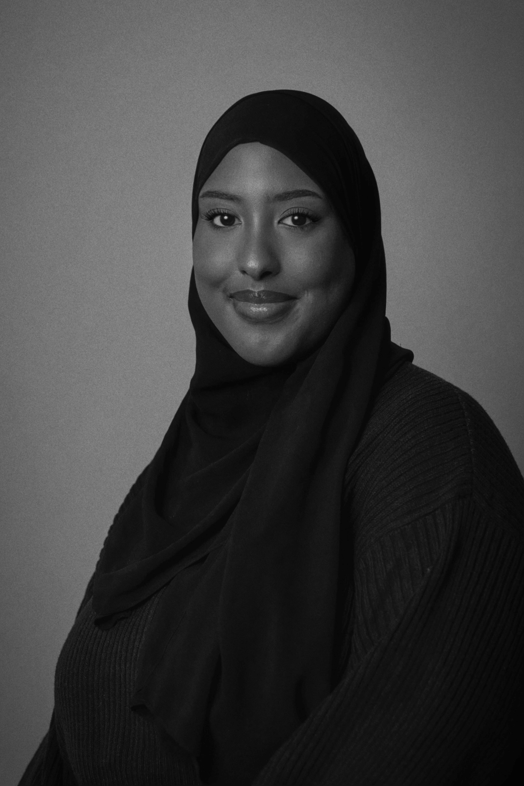 A headshot featuring a woman of color wearing a hijab and facing the camera