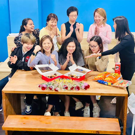 Asian women sitting around a wood table on which there are snacks and flowers to show appreciation.