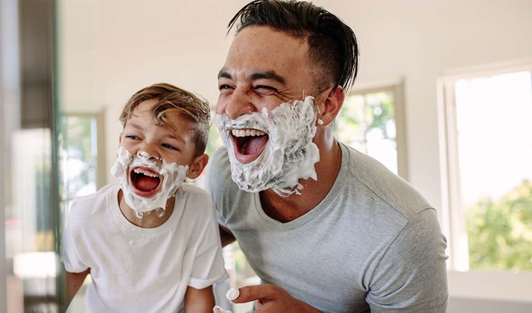 Caucasian father and son laugh at themselves in the mirror covered with shaving cream