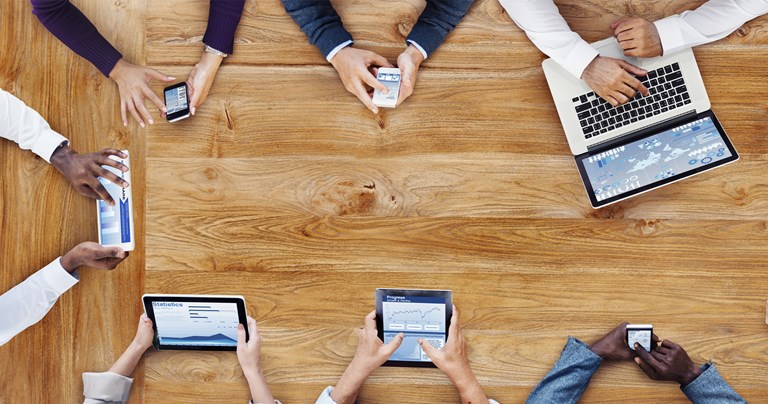 Hands holding tablets and phones sitting around a table