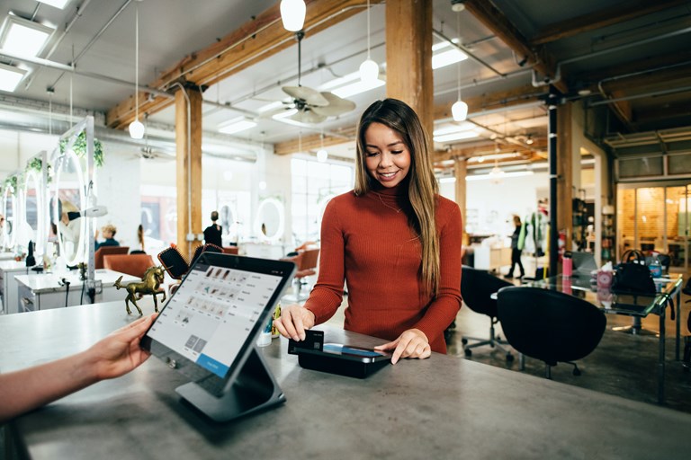 Woman in red top accepts card payment in front of digital screen