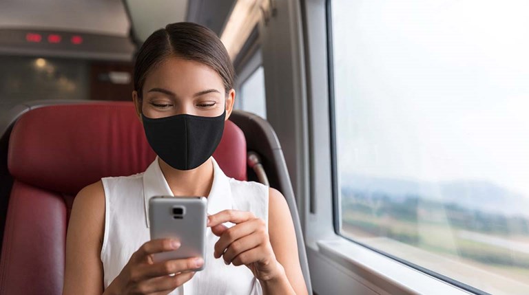 Asian woman wearing a mask and looking at mobile phone while riding a train
