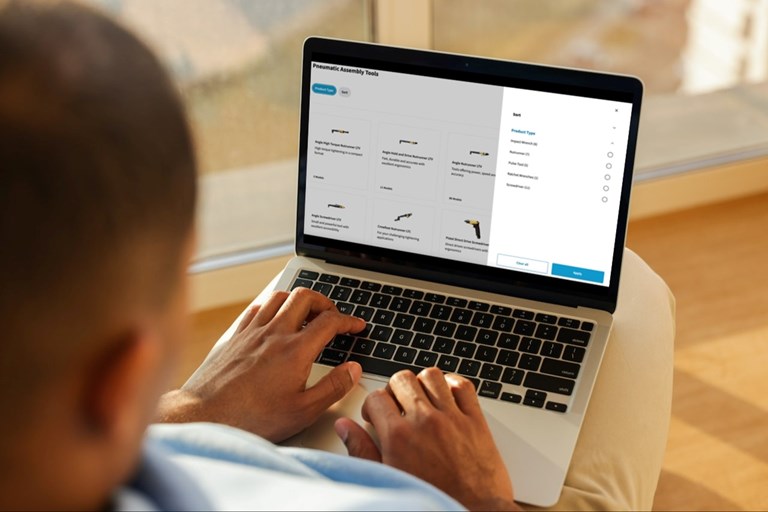 Person with a laptop on their lap and a screen showing a product review page for a drill on Atlas Copco's platform
