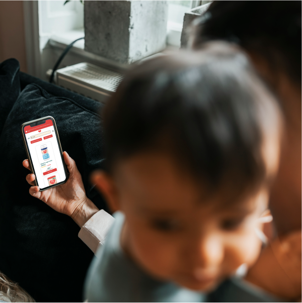 Parent on a sofa holding a phone with a Danone baby formula product page; baby blurred in the foreground. 