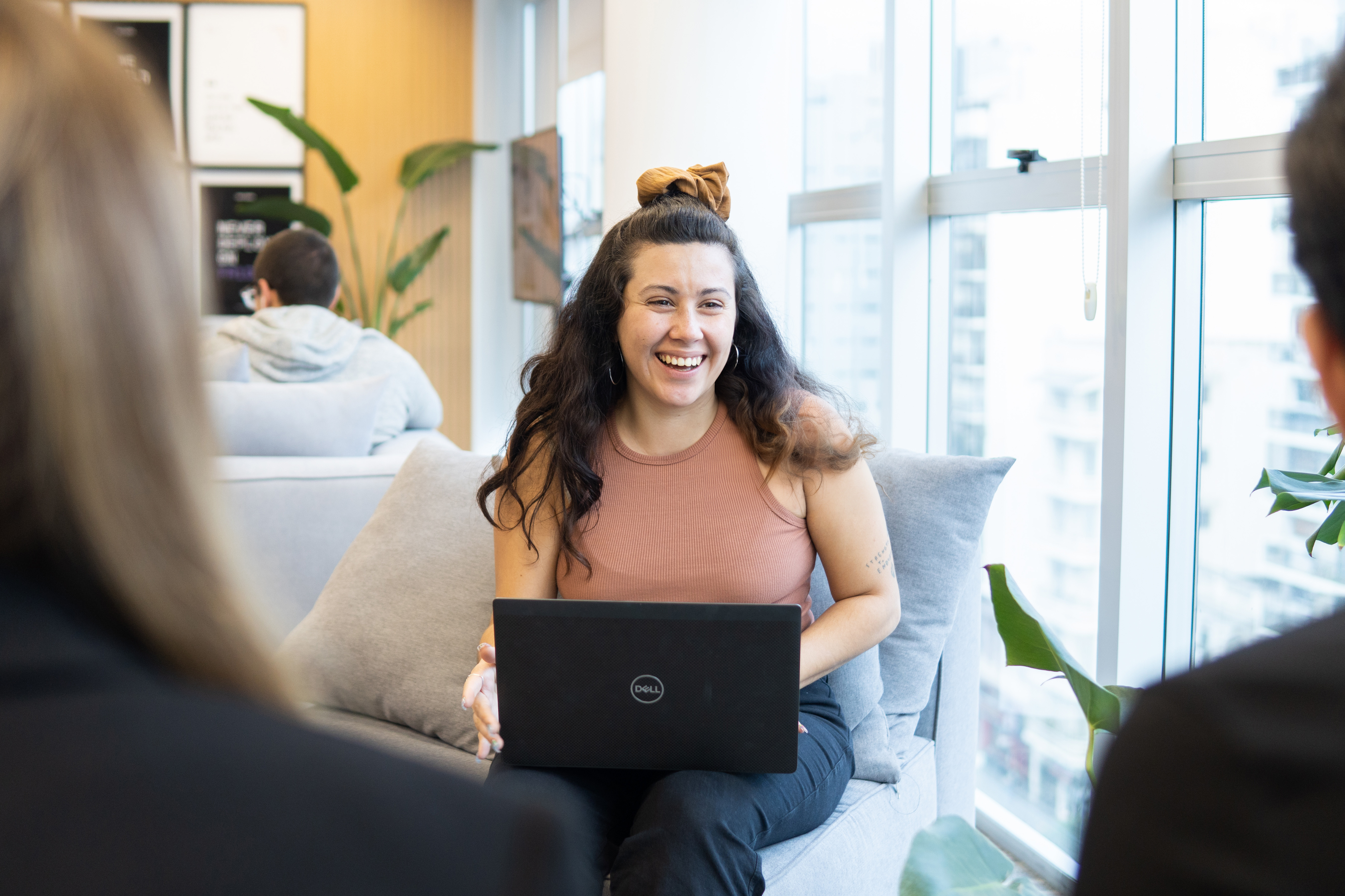 4 people in an office talking. The main focus is on a man with glasses and brown hair and a woman with red hair, smiling at a laptop