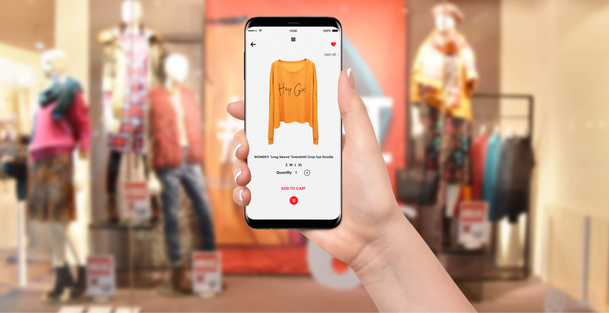 A hand holding a smartphone shows an online shopping app displaying a women’s “Hey Girl” sweatshirt for purchase. In the background, a blurred retail store window showcases mannequins dressed in colorful outfits, reinforcing the connection between physical and digital shopping experiences. The interface on the phone highlights product details such as size options, quantity, and the “Add to Cart” button.
