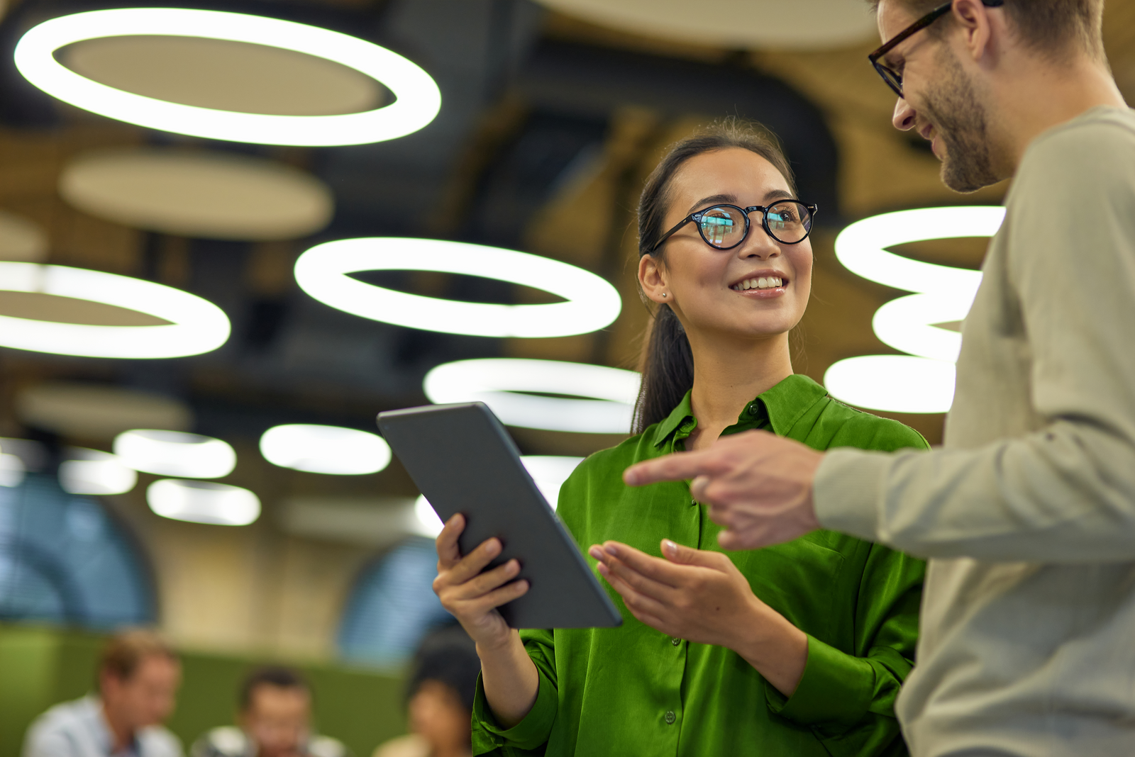 Two colleagues discussing work while holding a tablet in a modern office with circular lights