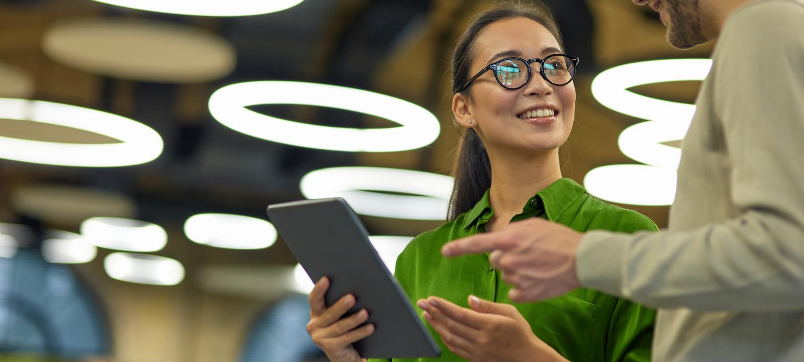 Two colleagues discussing work while holding a tablet in a modern office with circular lights