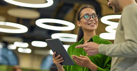 Two colleagues discussing work while holding a tablet in a modern office with circular lights