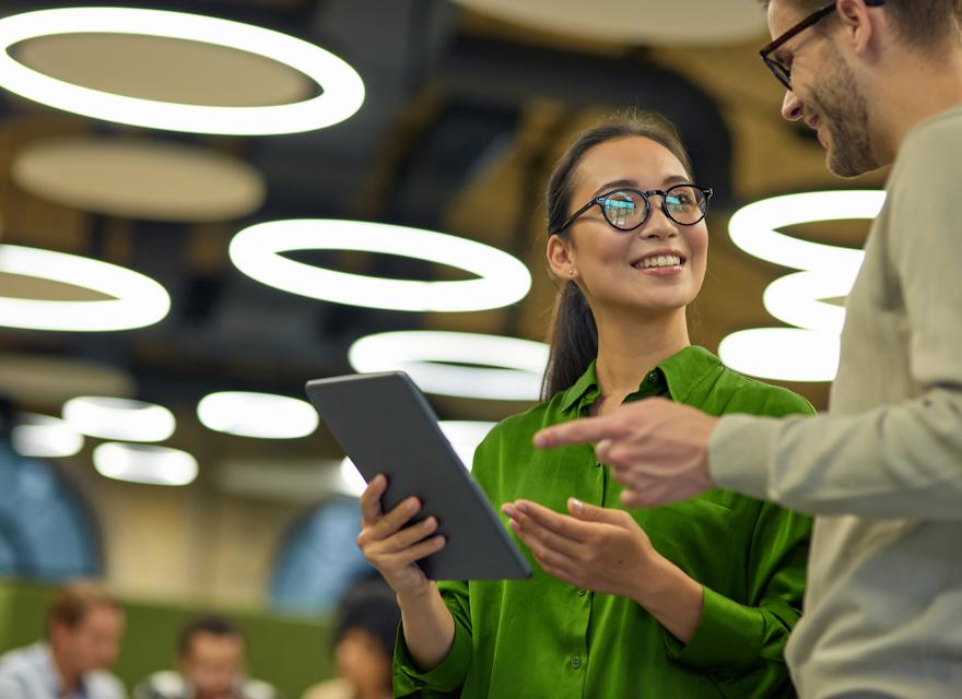 Two colleagues discussing work while holding a tablet in a modern office with circular lights