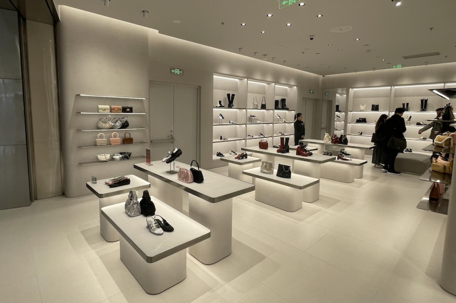 White luxury store displaying shoes and handbags on minimalist shelves and tables