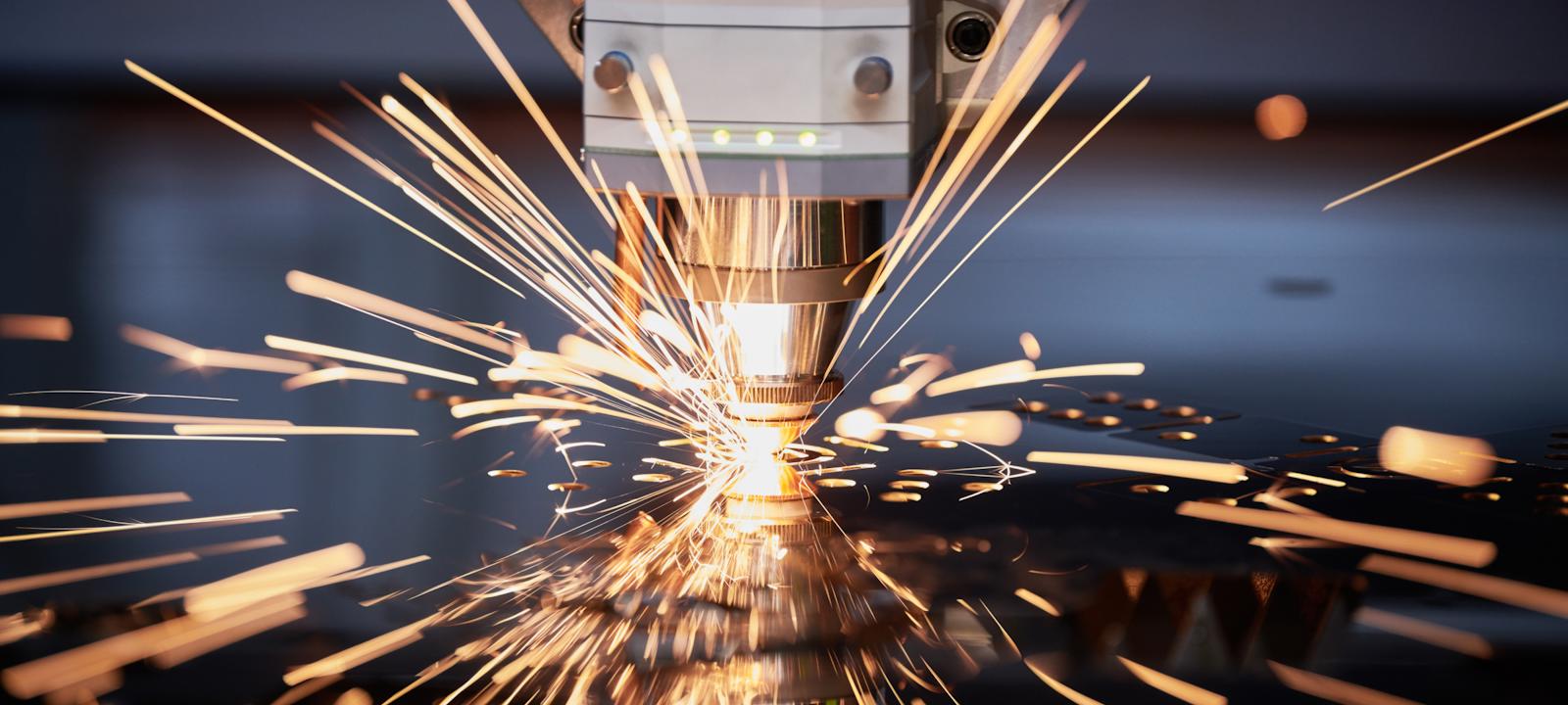 A close-up view of a laser cutting machine in action, emitting bright, golden sparks as it cuts through metal with precision. The machinery is detailed, with sharp focus on the nozzle and spark trails, creating a dynamic industrial scene.