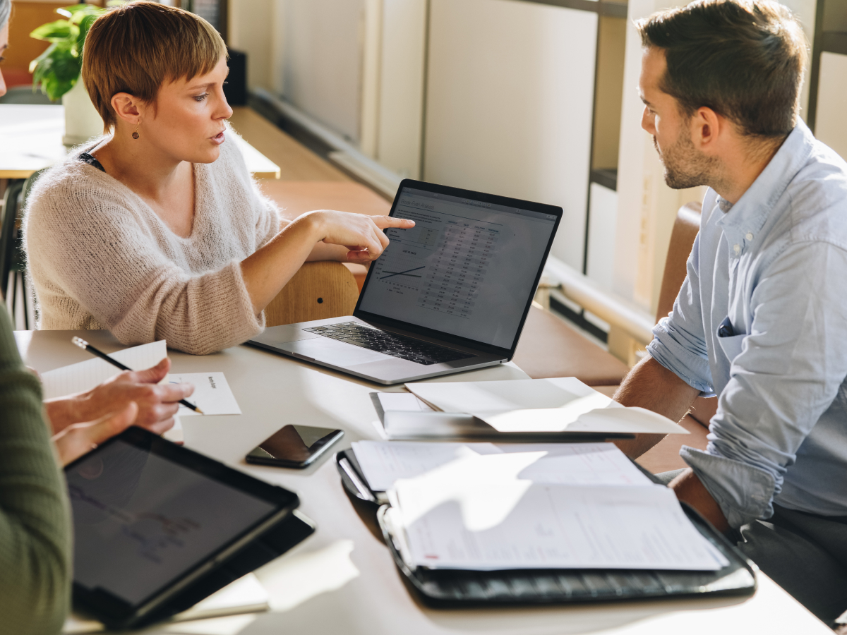 A group of five people is engaged in a discussion around a table with laptops