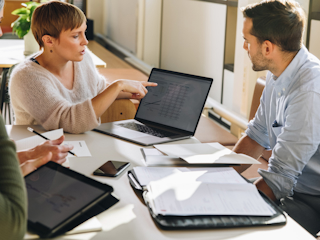A group of five people is engaged in a discussion around a table with laptops