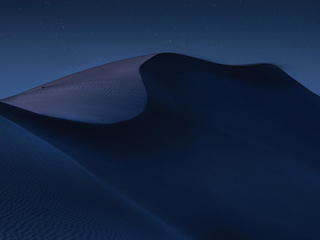 A serene nighttime landscape of desert dunes, softly illuminated under a clear, starry sky. The smooth curves and shadows of the sand create a dramatic, peaceful scene. The image captures the vastness and beauty of the desert under the calmness of night, evoking a sense of solitude and tranquility.
