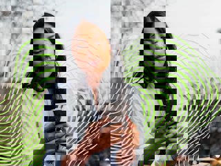 A woman sits outdoors, looking at her phone, dressed in a white shirt and beige pants, with sneakers