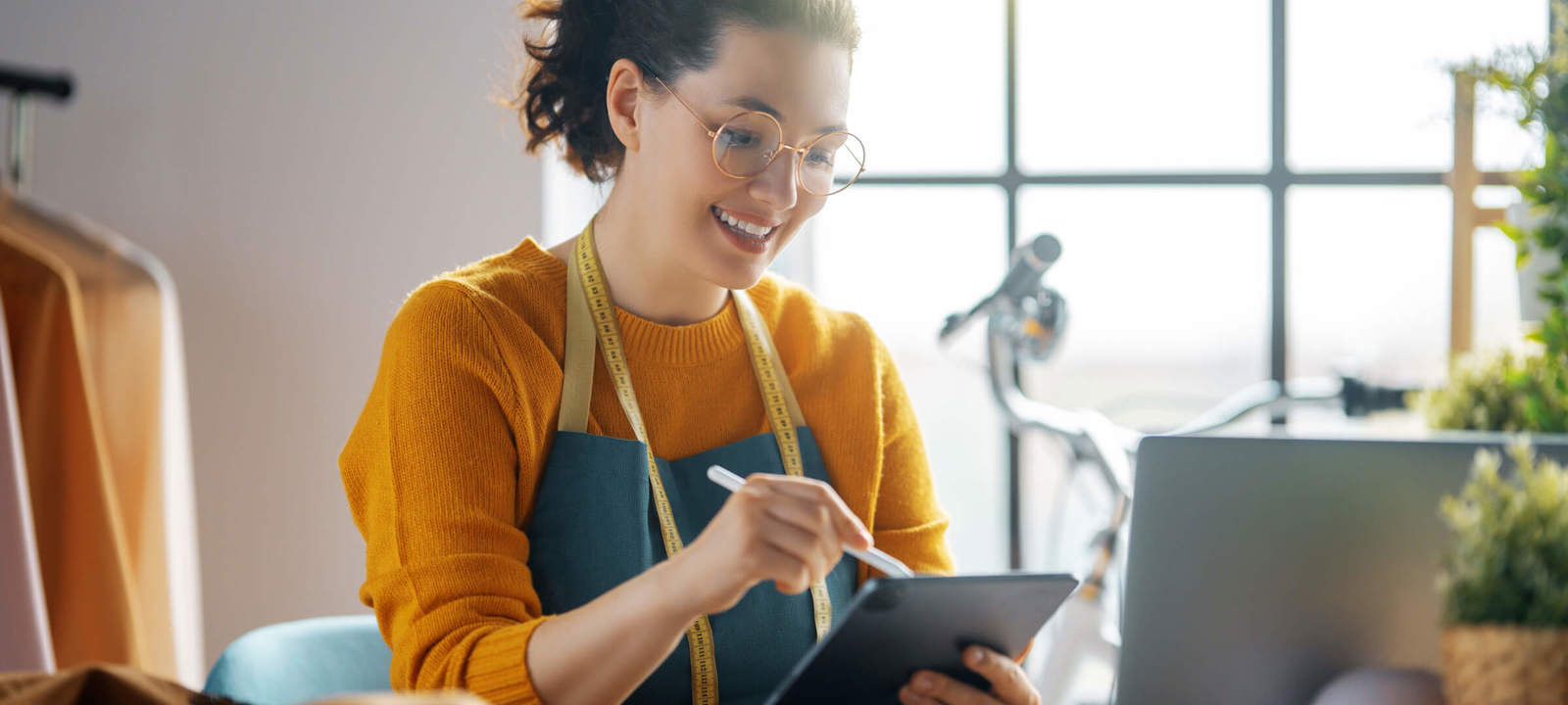 Tailor using a tablet while working in a bright, modern workspace.