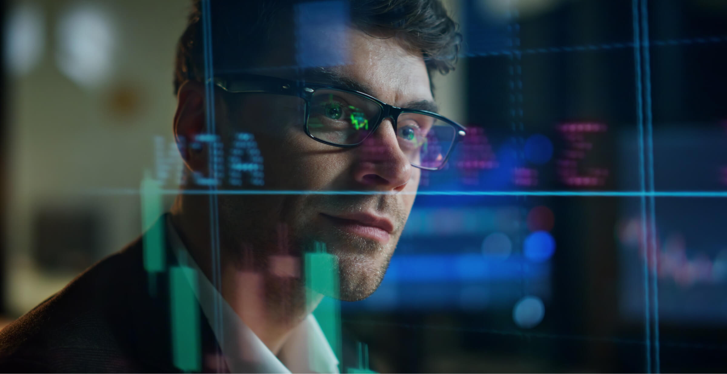 Man wearing glasses analyzing stock market data displayed on a digital screen with graphs and charts