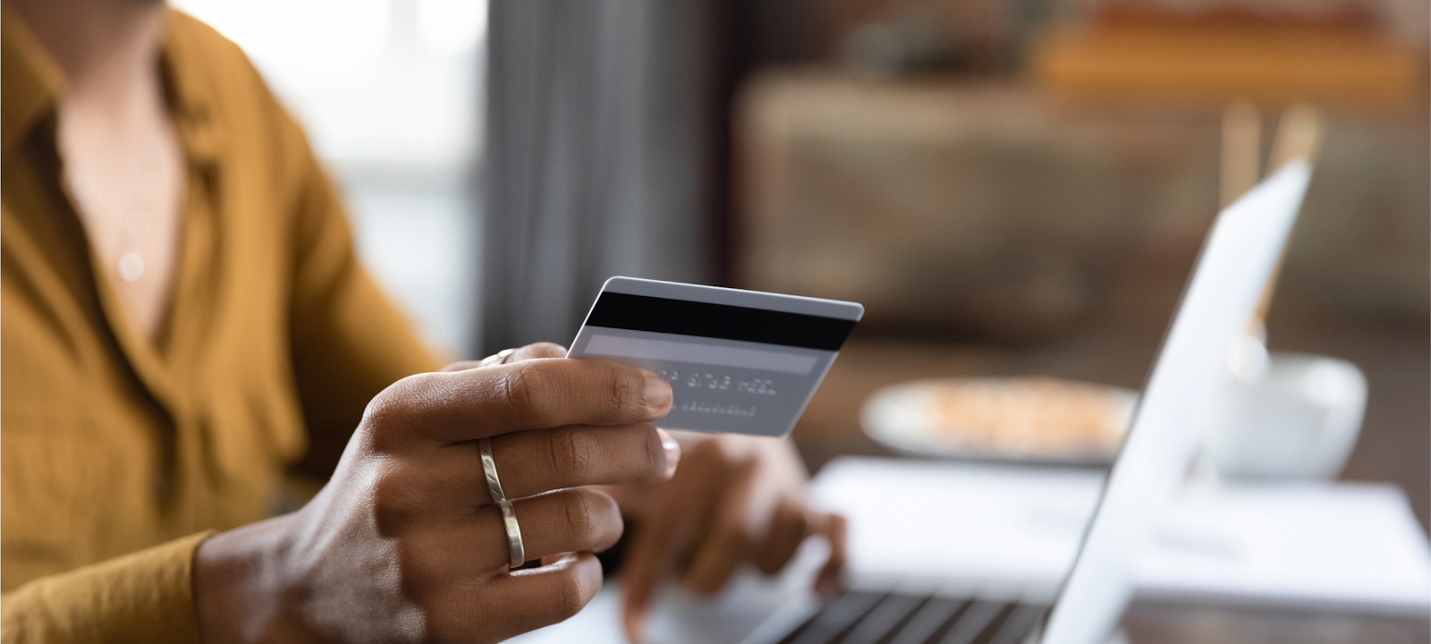 A close-up of a person holding a credit card while making an online purchase using a laptop. The person is typing with one hand and holding the card with the other, suggesting an online transaction or banking activity. The scene conveys the convenience and efficiency of digital financial services in a modern setting.
