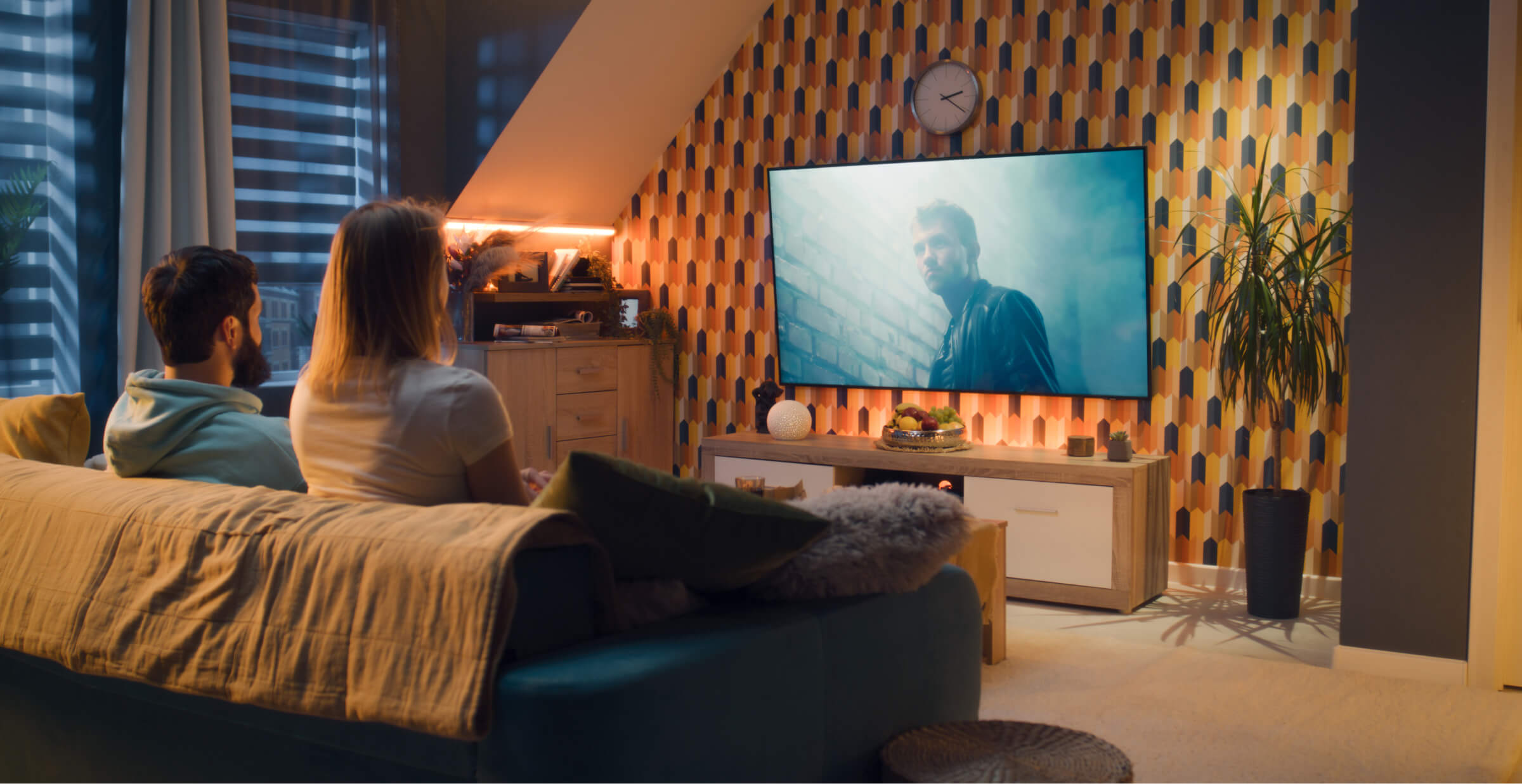 Couple sitting on a sofa in a modern living room, watching a movie on a large TV screen