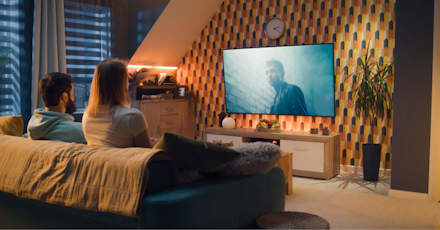 Couple sitting on a sofa in a modern living room, watching a movie on a large TV screen