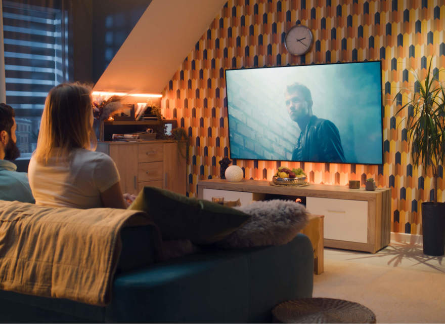 Couple sitting on a sofa in a modern living room, watching a movie on a large TV screen