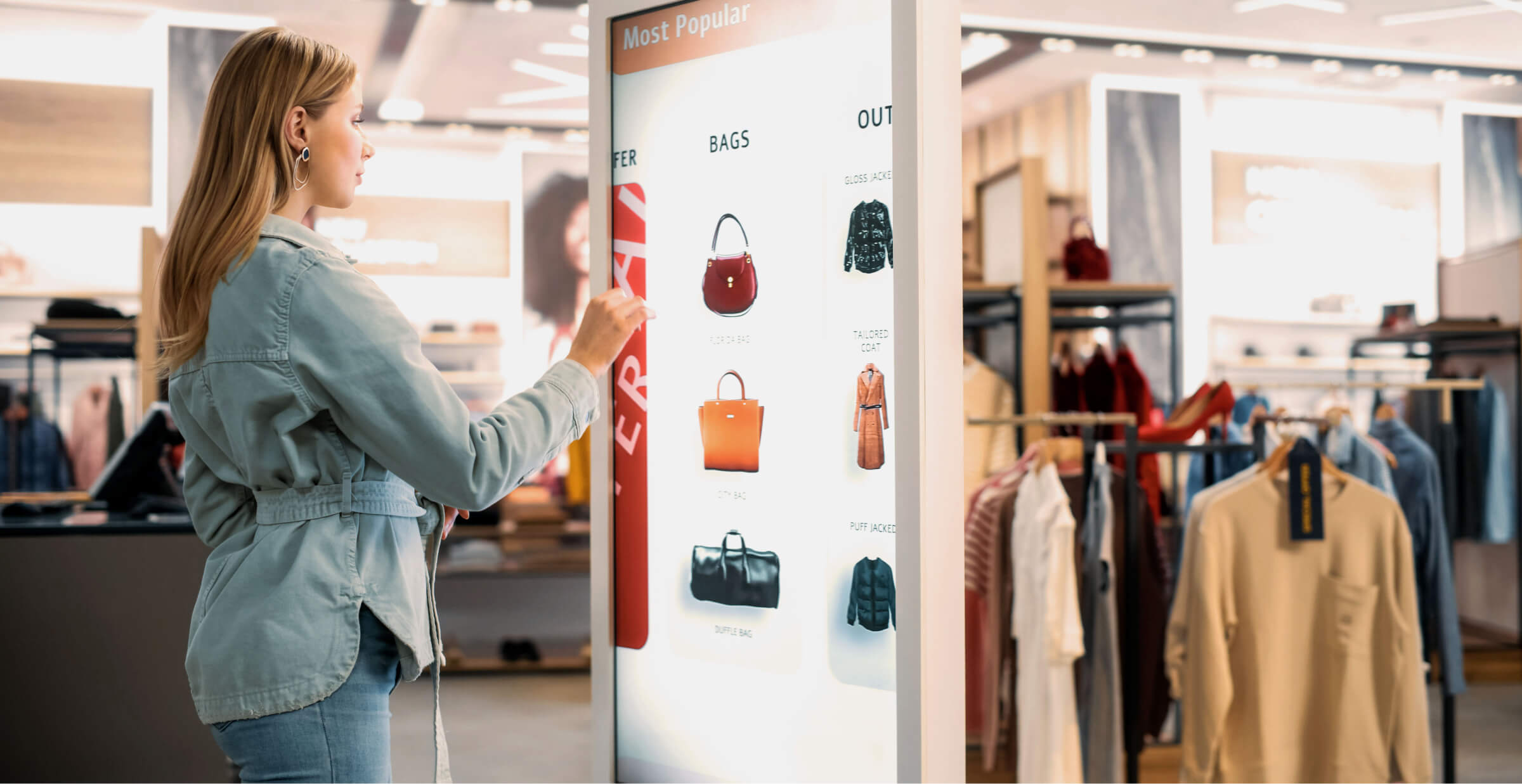 Woman using an interactive digital kiosk to browse handbags in a modern retail store.