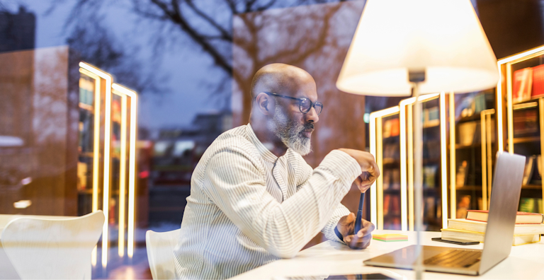 A man sitting at a desk in a modern well-lit library or study space.