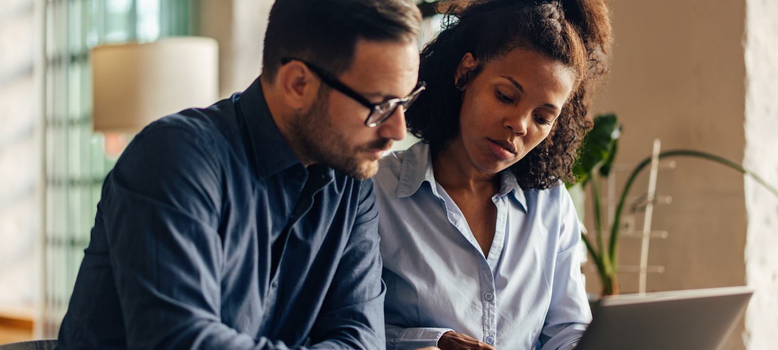 Two professionals collaborating at a table, reviewing documents on a laptop in a well-lit modern office space.