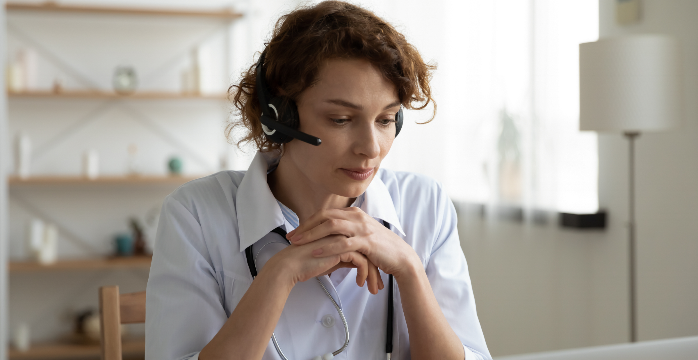 A doctor wearing a headset and stethoscope, sitting at a desk and engaging in a virtual consultation.