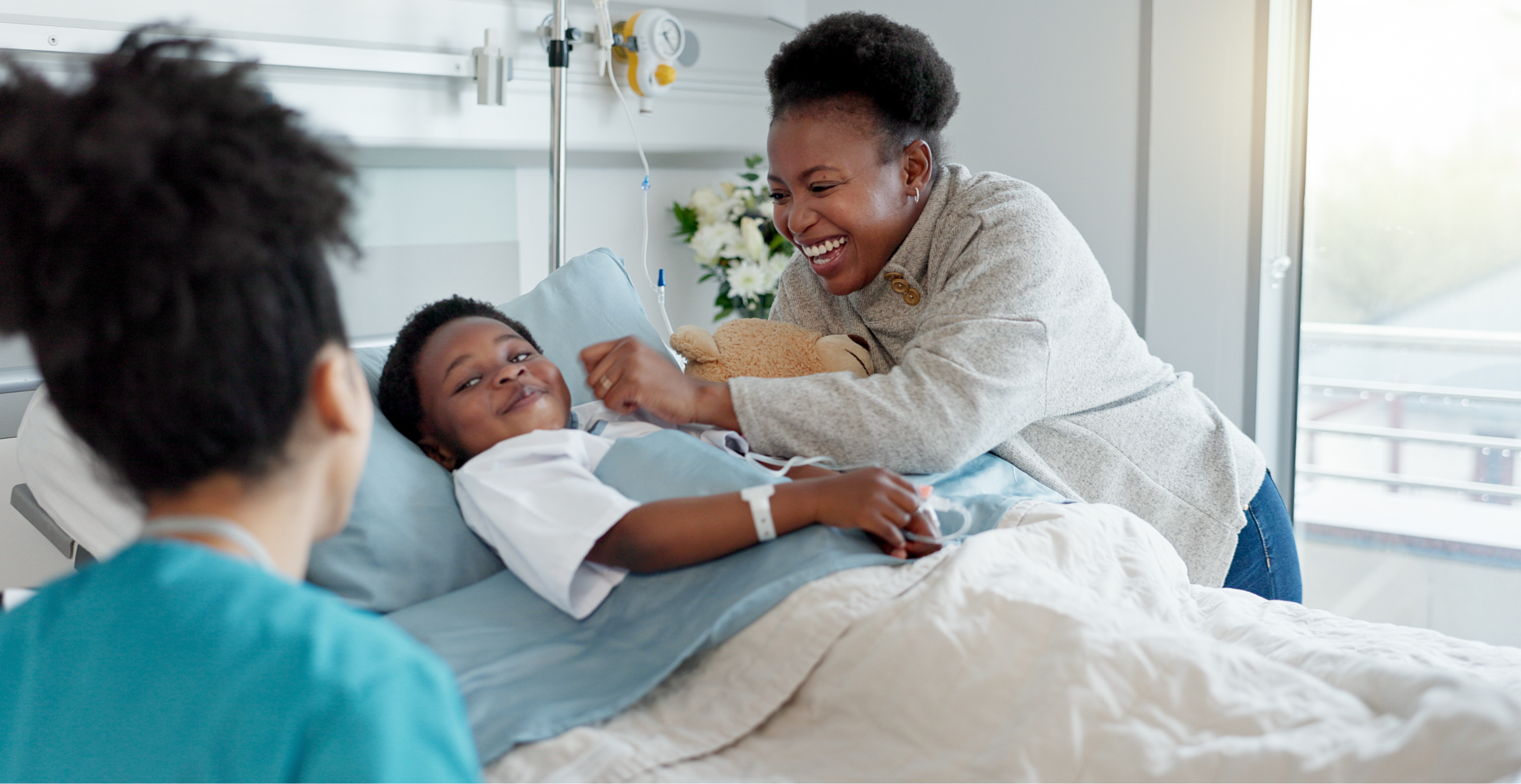 A cheerful hospital scene with a young patient in bed, smiling alongside a parent and a healthcare professional nearby.