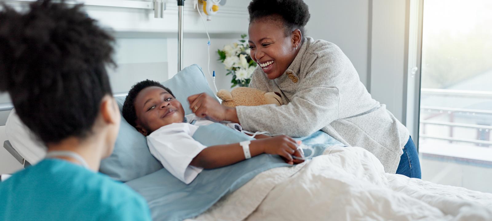 A cheerful hospital scene with a young patient in bed, smiling alongside a parent and a healthcare professional nearby.