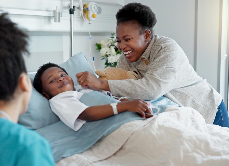 A cheerful hospital scene with a young patient in bed, smiling alongside a parent and a healthcare professional nearby.