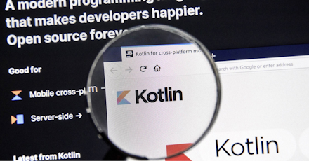 A close-up of a computer screen showing the Kotlin programming language website through a magnifying glass. The screen highlights that Kotlin is a modern, open-source programming language, with emphasis on mobile cross-platform and server-side development. The magnified section focuses on the Kotlin logo, reinforcing its relevance in the developer community. The image represents the importance of Kotlin in modern software development.