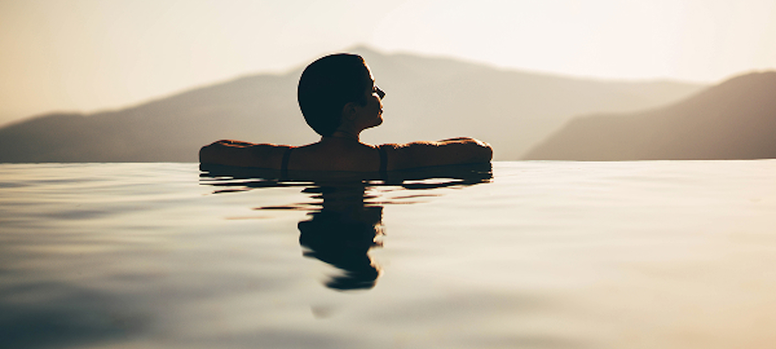 A woman wading in the water during a vibrant sunset, with warm colors reflecting on the surface