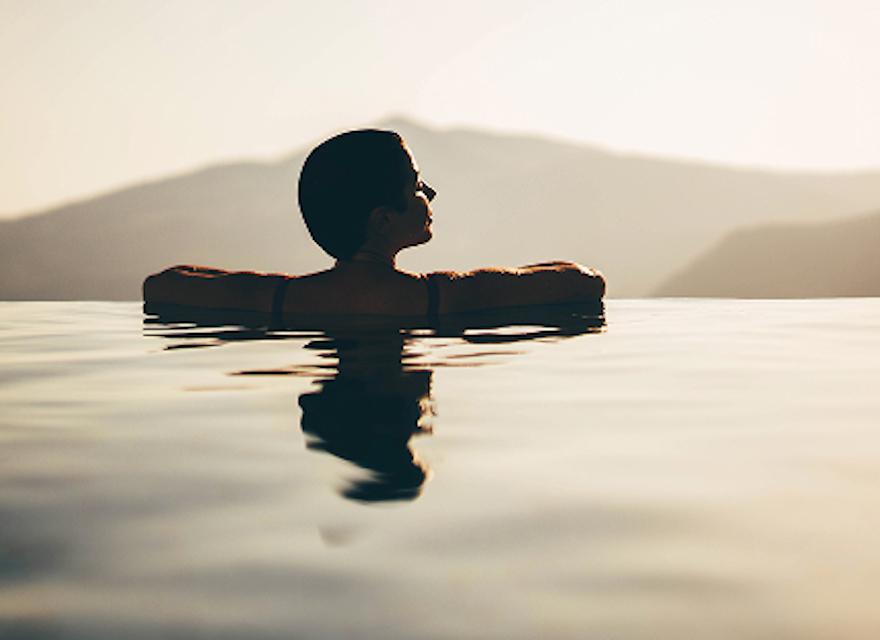 A woman wading in the water during a vibrant sunset, with warm colors reflecting on the surface