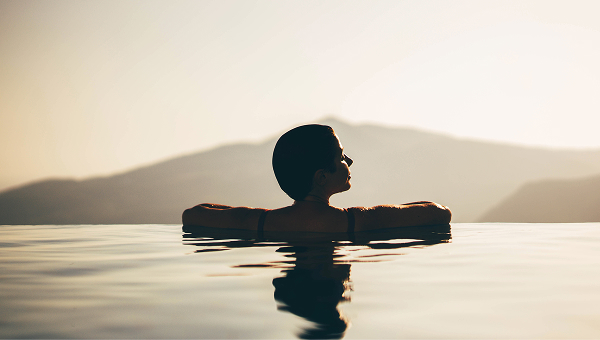 A woman wading in the water during a vibrant sunset, with warm colors reflecting on the surface