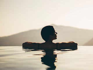 A woman wading in the water during a vibrant sunset, with warm colors reflecting on the surface