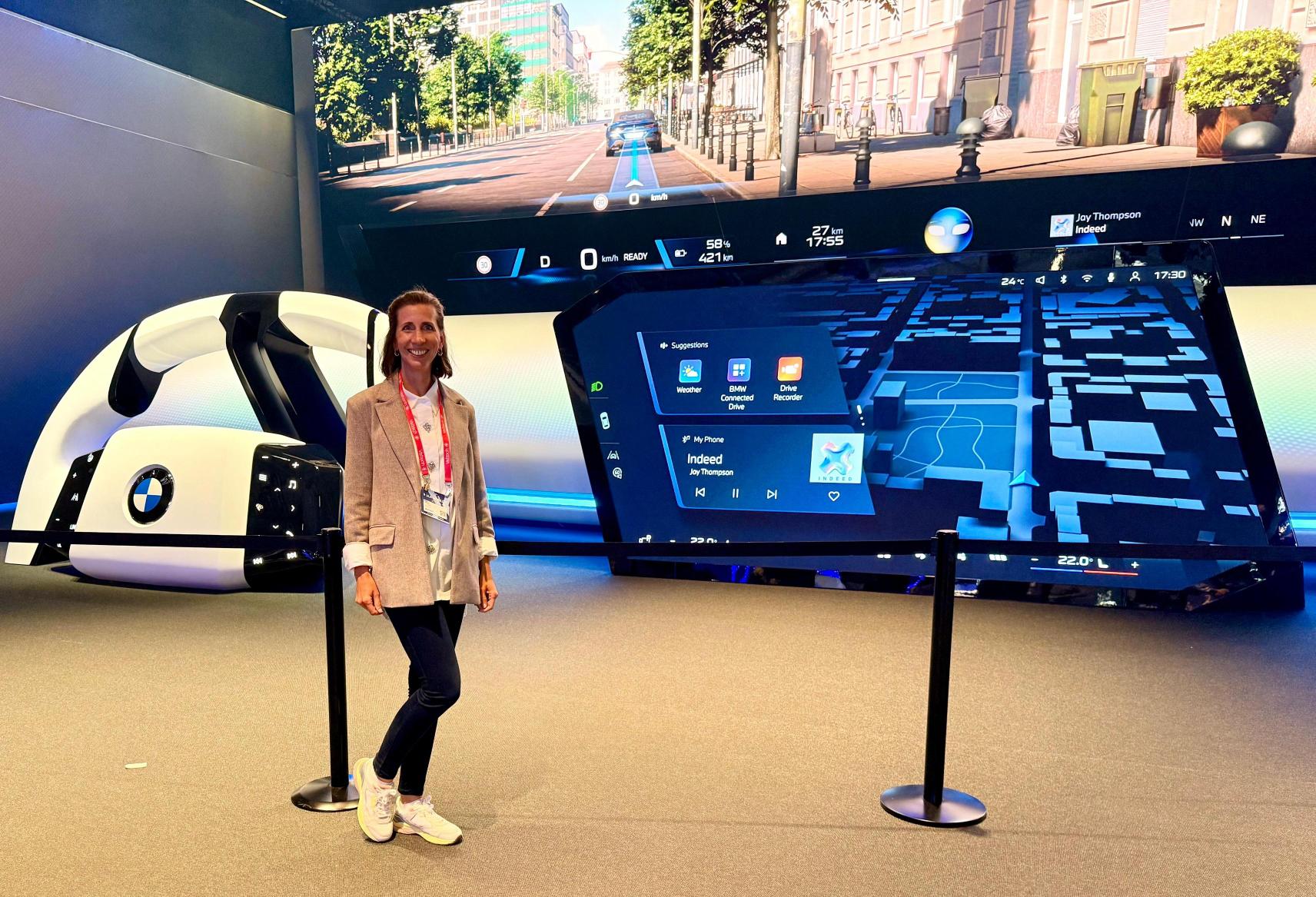 A woman stands in front of a large screen, engaged in a presentation or discussion. 