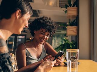 Two women sitting at a table, focused on their phones while enjoying each other's company.