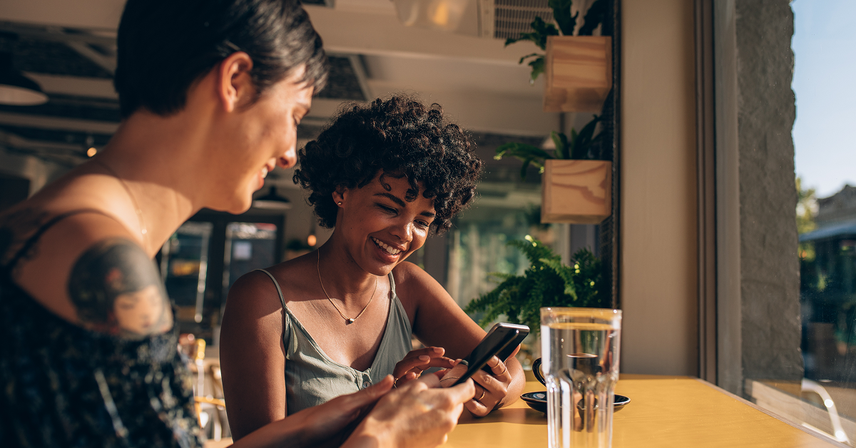 Two women sitting at a table, focused on their phones while enjoying each other's company.