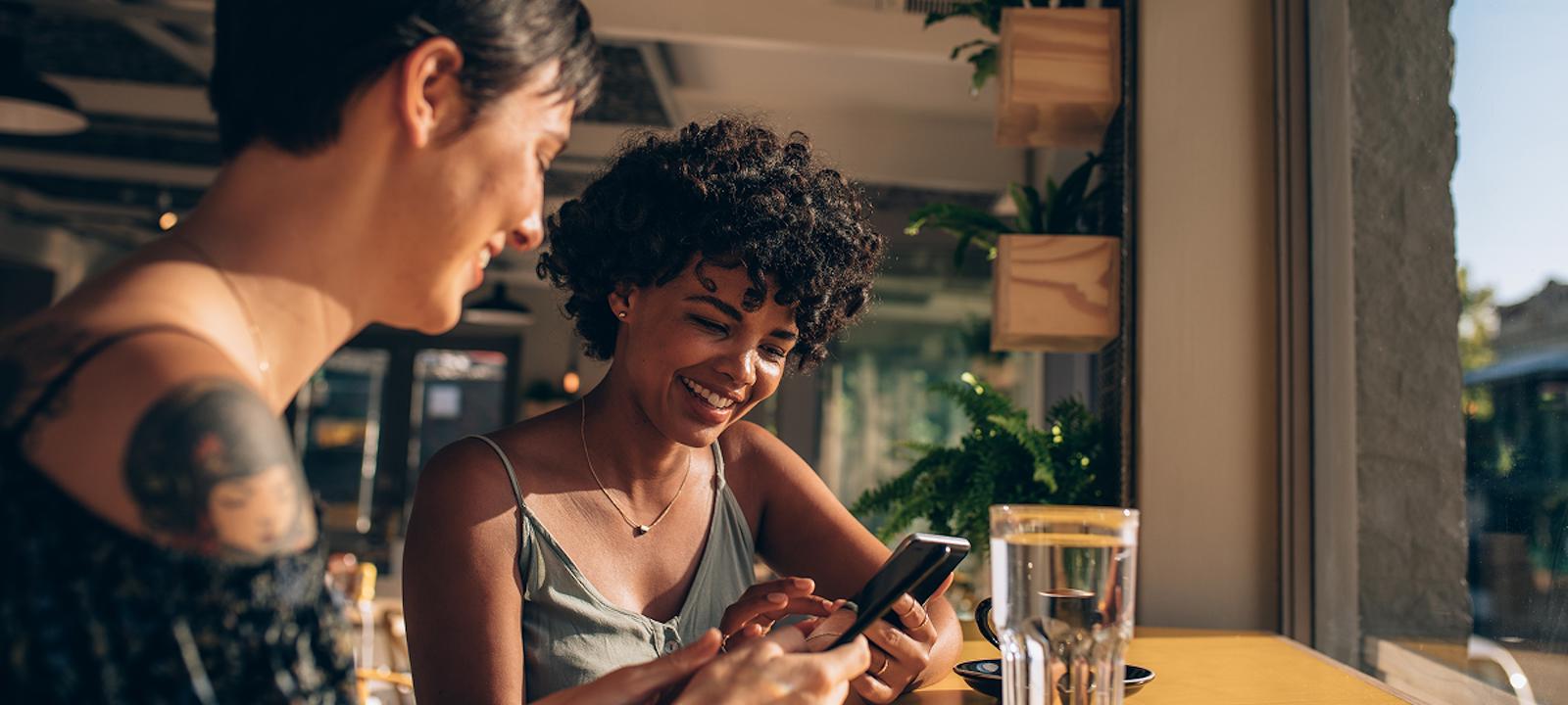 Two women sitting at a table, focused on their phones while enjoying each other's company.