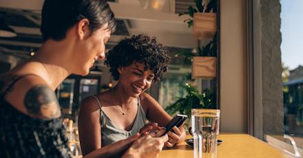 Two women sitting at a table, focused on their phones while enjoying each other's company.