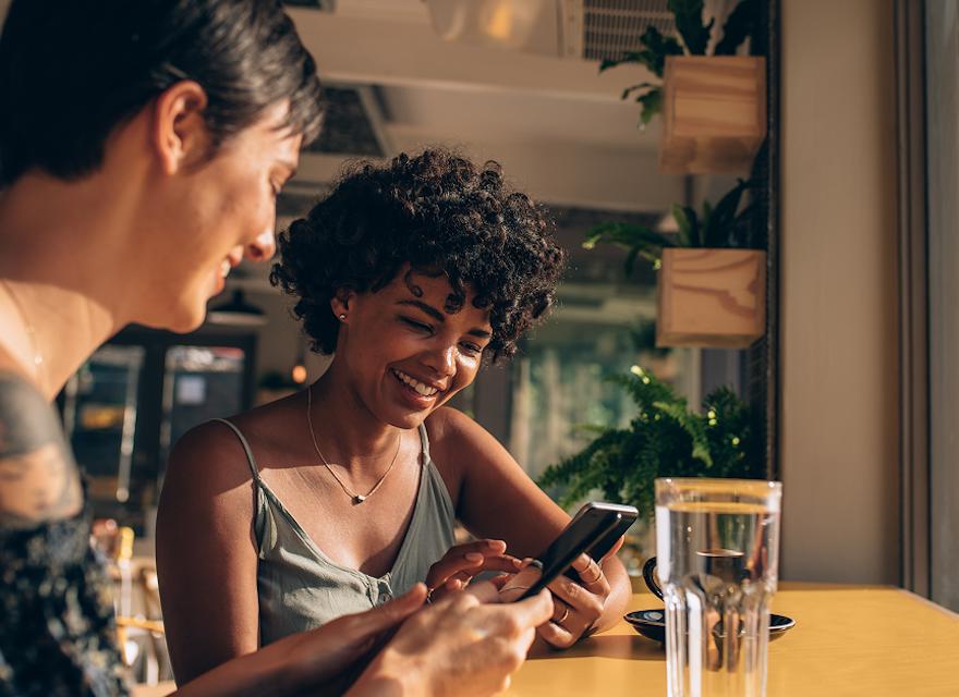 Two women sitting at a table, focused on their phones while enjoying each other's company.