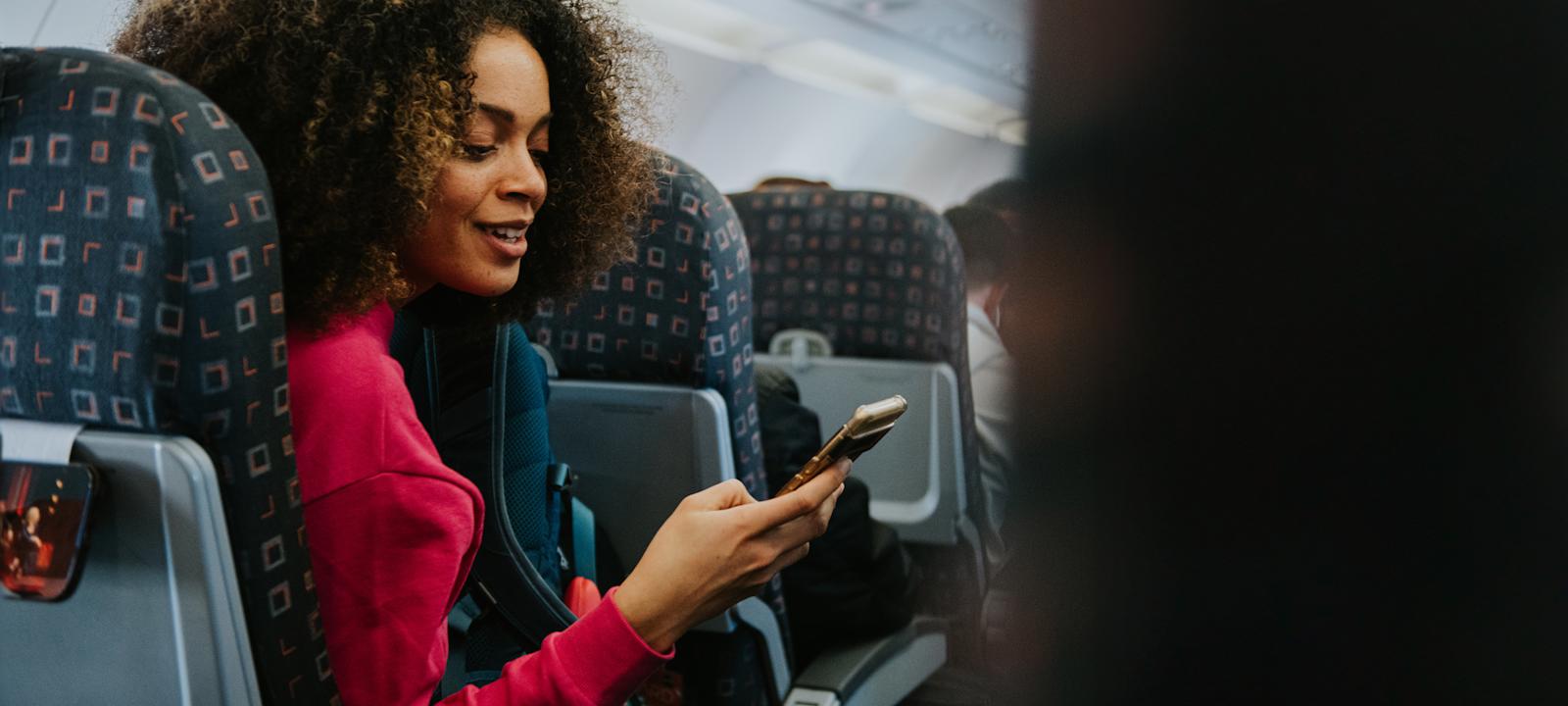 A woman sitting on an airplane, focused on her phone while enjoying her flight