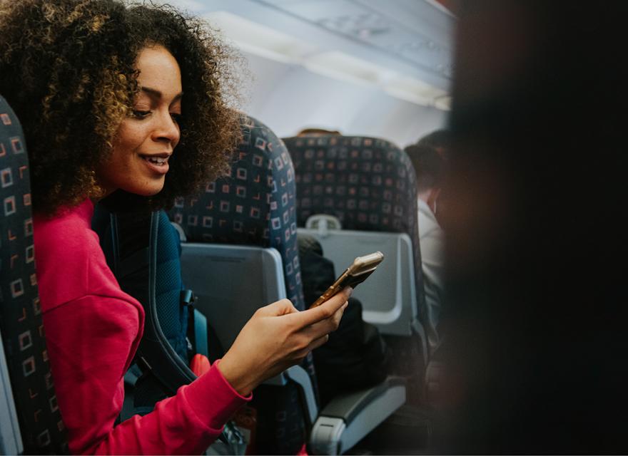 A woman sitting on an airplane, focused on her phone while enjoying her flight