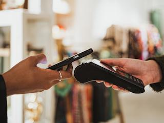 A person holds a cell phone in one hand and a credit card in the other, ready to make a transaction.