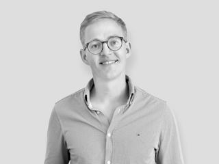 A smiling man wearing glasses and a shirt, exuding a friendly and approachable vibe.